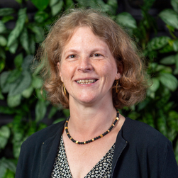 A headshot of a smiling woman with neck-length auburn hair, wearing a neckless