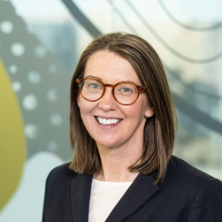 A headshot of a smiling woman wearing glasses with shoulder-length brown hair