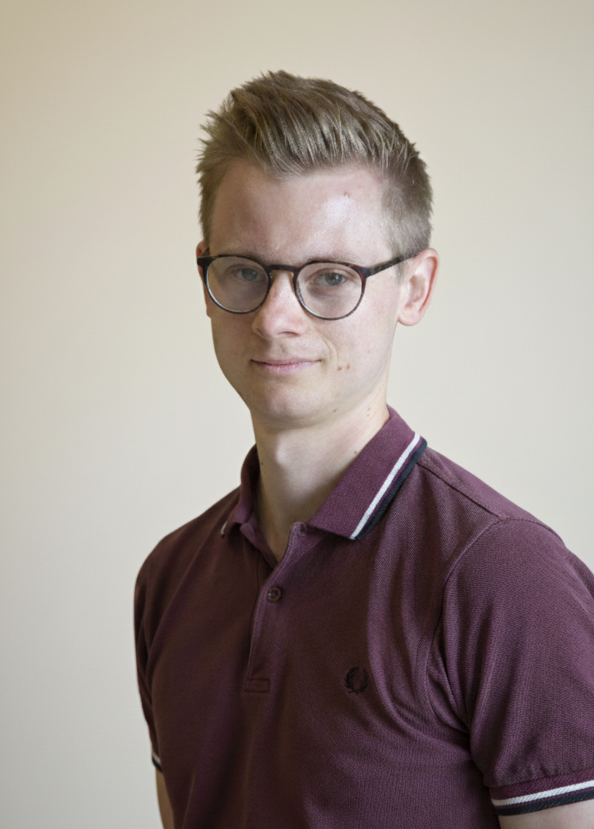 A man with blonde hair and glasses, wearing a burgundy polo shirt.