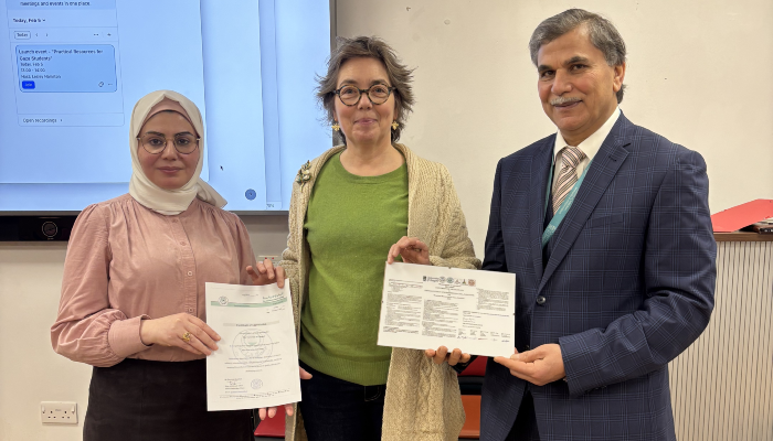Olwyn Byron (centre), Adnan Al-Hindi (right) and an academic colleague (left) stood together in the SGDB Level 2 room, holding educational resources in front of a screen during the Life Sciences Resources for Gaza launch event.