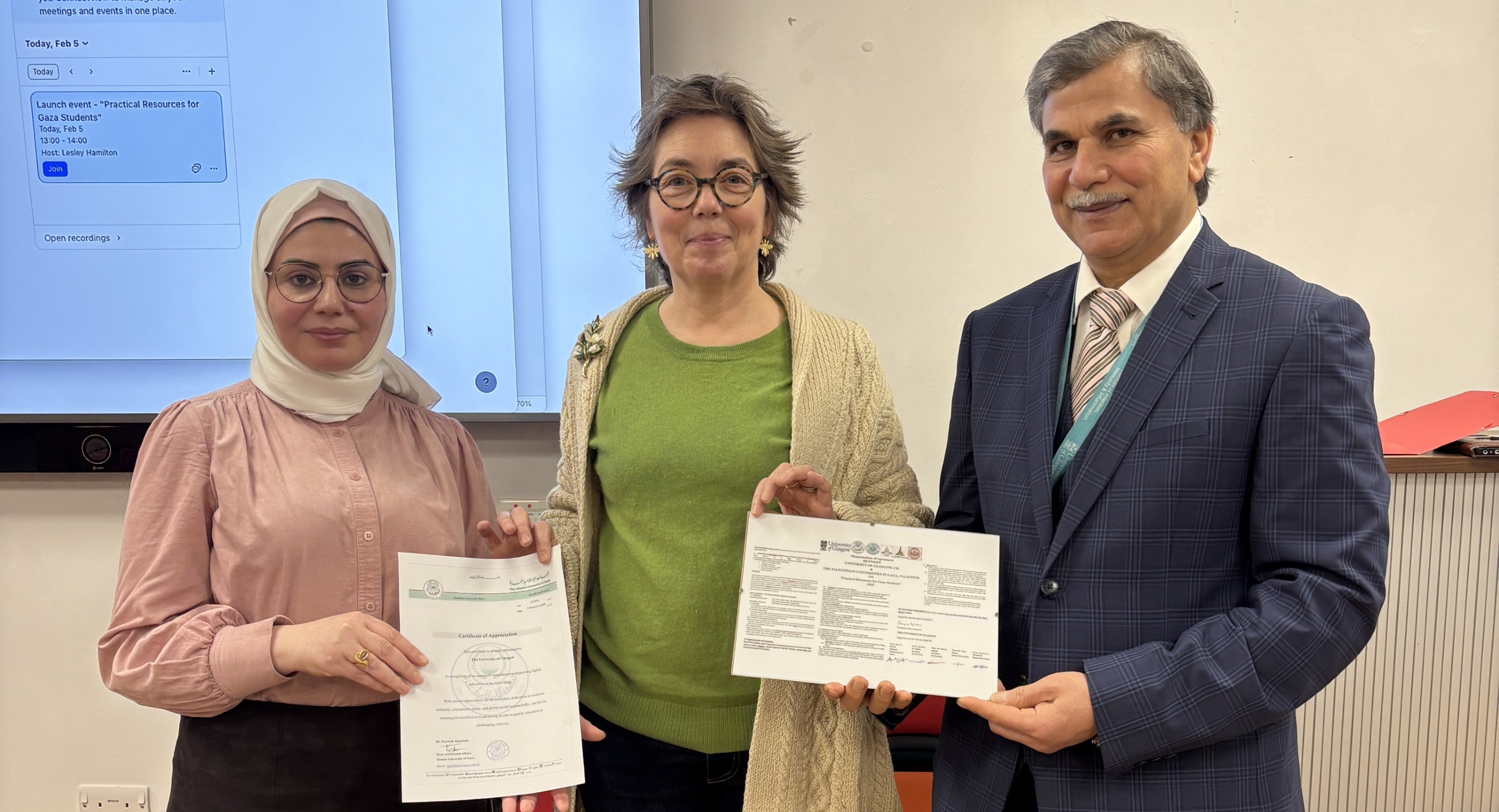 Olwyn Byron (centre), Adnan Al-Hindi (right) and an academic colleague (left) stood together in the SGDB Level 2 room, holding educational resources in front of a screen during the Life Sciences Resources for Gaza launch event.