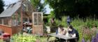 students sit at a picnic table in a flower garden next to a green house