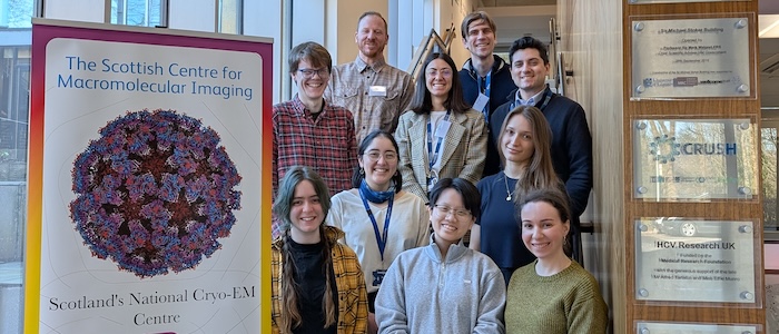 6 women and 4 men stood posing on a staircase next to a floor-to-ceiling window. A promotional SCMI pop-up banner is in the foreground.