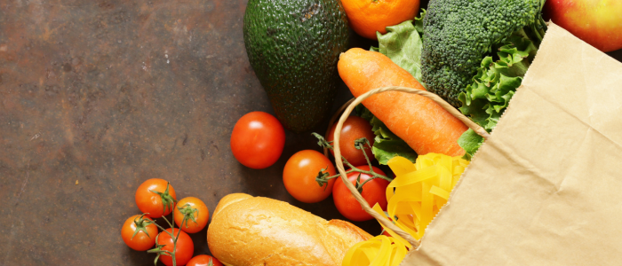 Food items spilling out of a paper grocery bag, including a baguette, an avocado, and tomatoes.