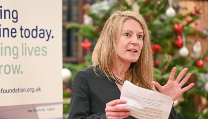 An image of Dr Eve Smith facing an audience and passionately presenting while holding a paper in one hand and gesturing with her other.