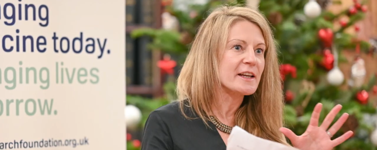 An image of Dr Eve Smith facing an audience and passionately presenting while holding a paper in one hand and gesturing with her other.