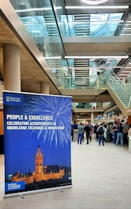 A banner saying People and Excellence in front of the corridor; a group of people stands at the end of it.