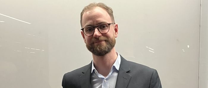 Eamon smiles at the camera, wearing a dark grey jacket and pale blue shirt.