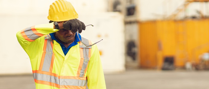 A tired worker in safety gear rubs his face.