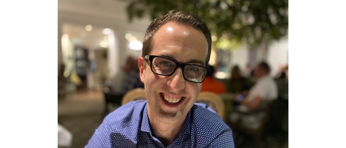 Professor Peter MacPherson smiling. He wears a blue shirt and glasses.