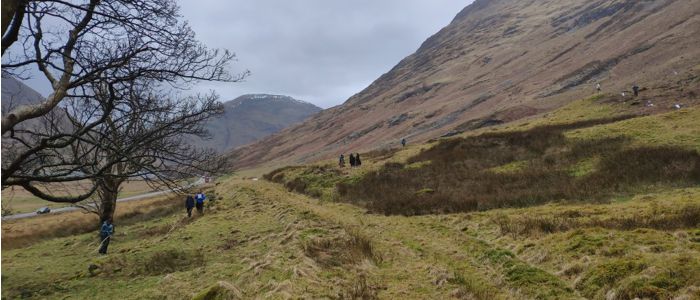 Groups of students looking at 19th century building complex and recent excavation sites at Glencoe