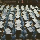 Overhead view of graduates seated in rows wearing caps and gowns, seen from behind during a graduation ceremony.
