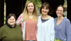 From left to right, Lesley Hamilton, Laura McCaughey, Fiona Stubbs, and Anna McGregor stand together outdoors beneath a stone archway, smiling at the camera. Trees and historic university buildings are visible in the background.