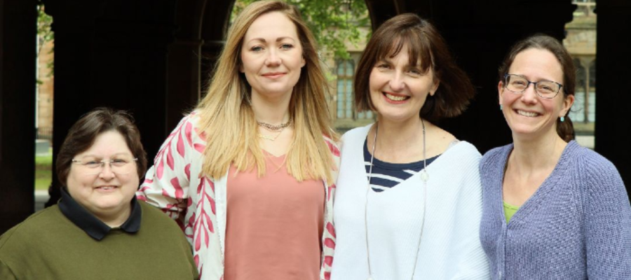 From left to right, Lesley Hamilton, Laura McCaughey, Fiona Stubbs, and Anna McGregor stand together outdoors beneath a stone archway, smiling at the camera. Trees and historic University buildings are visible in the background.