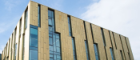 A modern multi-storey university research building with gold-toned metal cladding, tall vertical windows, and angular architectural details against a partly cloudy sky. The Sir Michael Stoker Building, home to the CVR, pictured on the University of Glasgow’s Garscube campus.