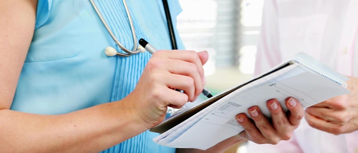 A clinician wearing a blue top and a stethescope is writing notes on a pad