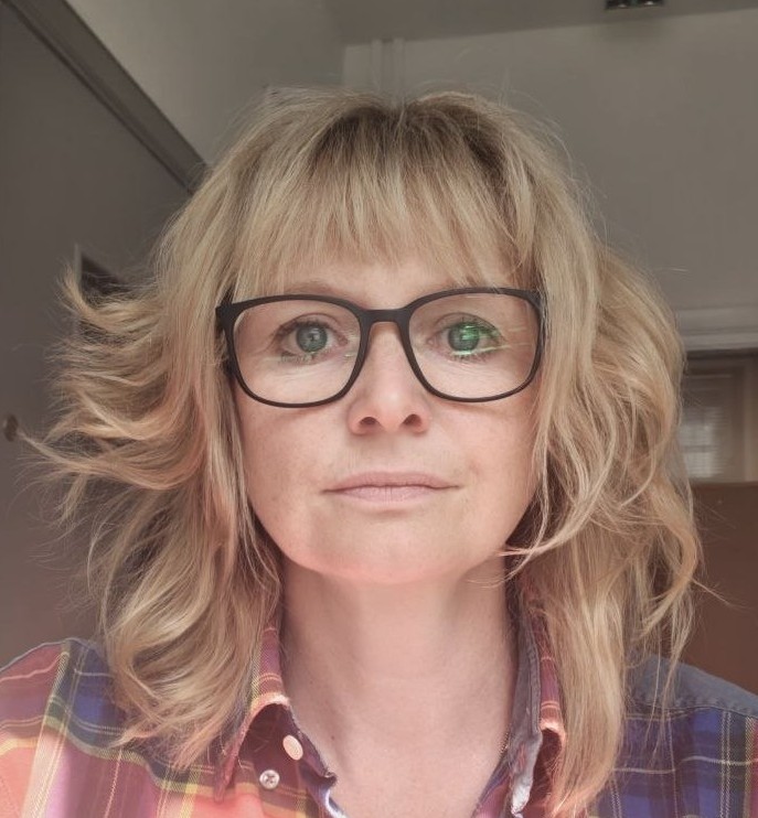 Staff page profile picture of a caucasian woman with blonde shoulder length hair, wearing balck framed glasses