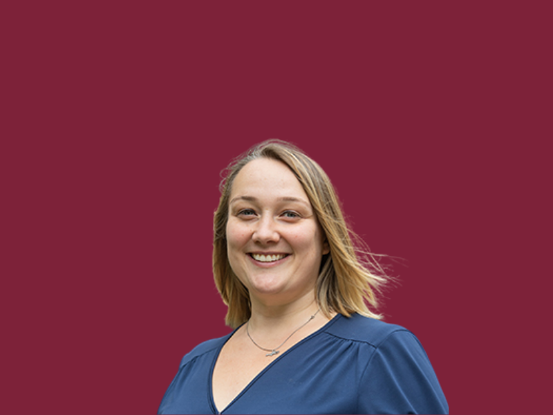 Professor Kat Riach headshot on a solid burgundy background