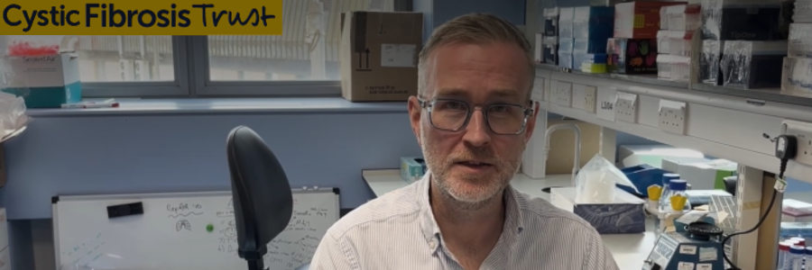 Professor Robert Gray sits in a laboratory at the University of Glasgow, facing the camera. Laboratory equipment, a whiteboard and workstations are visible in the background. The image includes the Cystic Fibrosis Trust logo and an on-screen caption identifying him as 