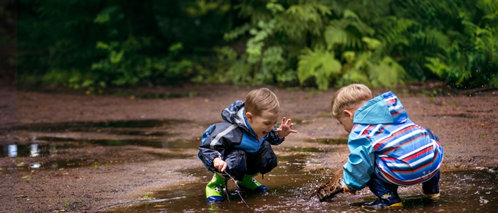 Two young boys are crouching down in a puddle of water playing