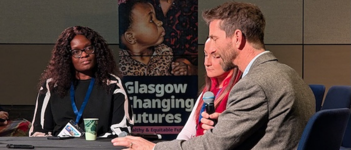Three people around the table, one - a male - is holding a microphone and speaking