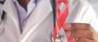 A doctor is holding a red ribbon which is the universal international symbol of HIV/AIDS awareness.