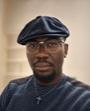 A black male wearing glasses and a dark hat