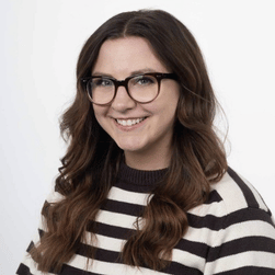 A headshot of a smiling woman wearing glasses with long dark hair, wearing stripy black and white jumper