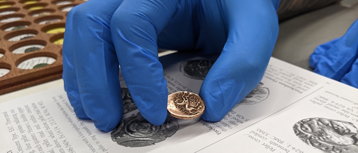 A researcher handles an ancient gold coin using a rubber glove