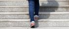 The legs of a person wearing blue jeans and trainers walking up stairs