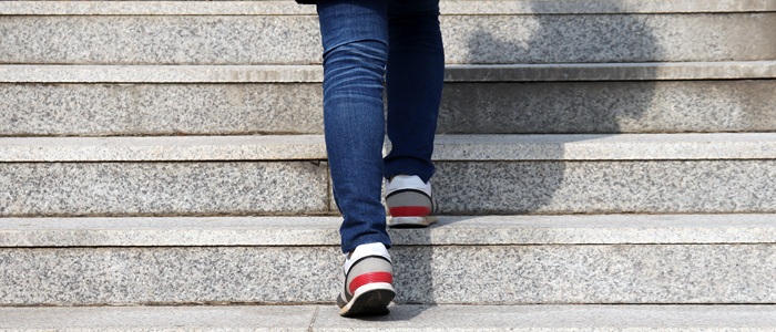 The legs of a person wearing blue jeans and trainers walking up stairs