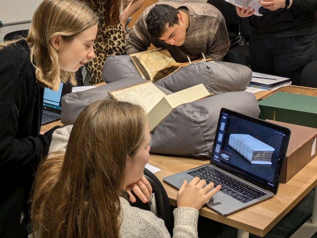 A set of students look at archival books and material on line.