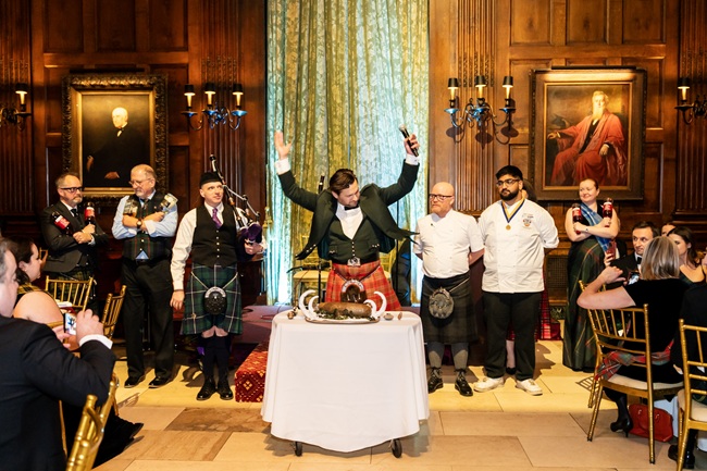 People stand around a table as a man cuts into a haggis for Burns Night
