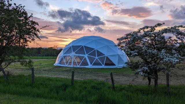 White, geodesic dome, marquee structure sitting in field at dusk