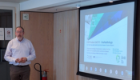 Professor Harry De Koning stands beside a projection screen while delivering a presentation at a European Cooperation in Science and Technology (COST) workshop on drug development.
