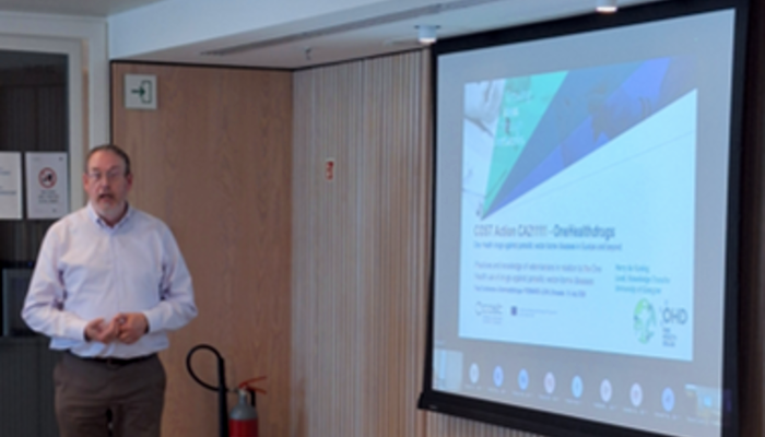 Professor Harry De Koning stands beside a projection screen while delivering a presentation at a European Cooperation in Science and Technology (COST) workshop on drug development.