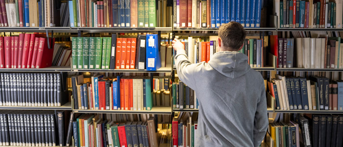 A student looking through shelves of books in the Library