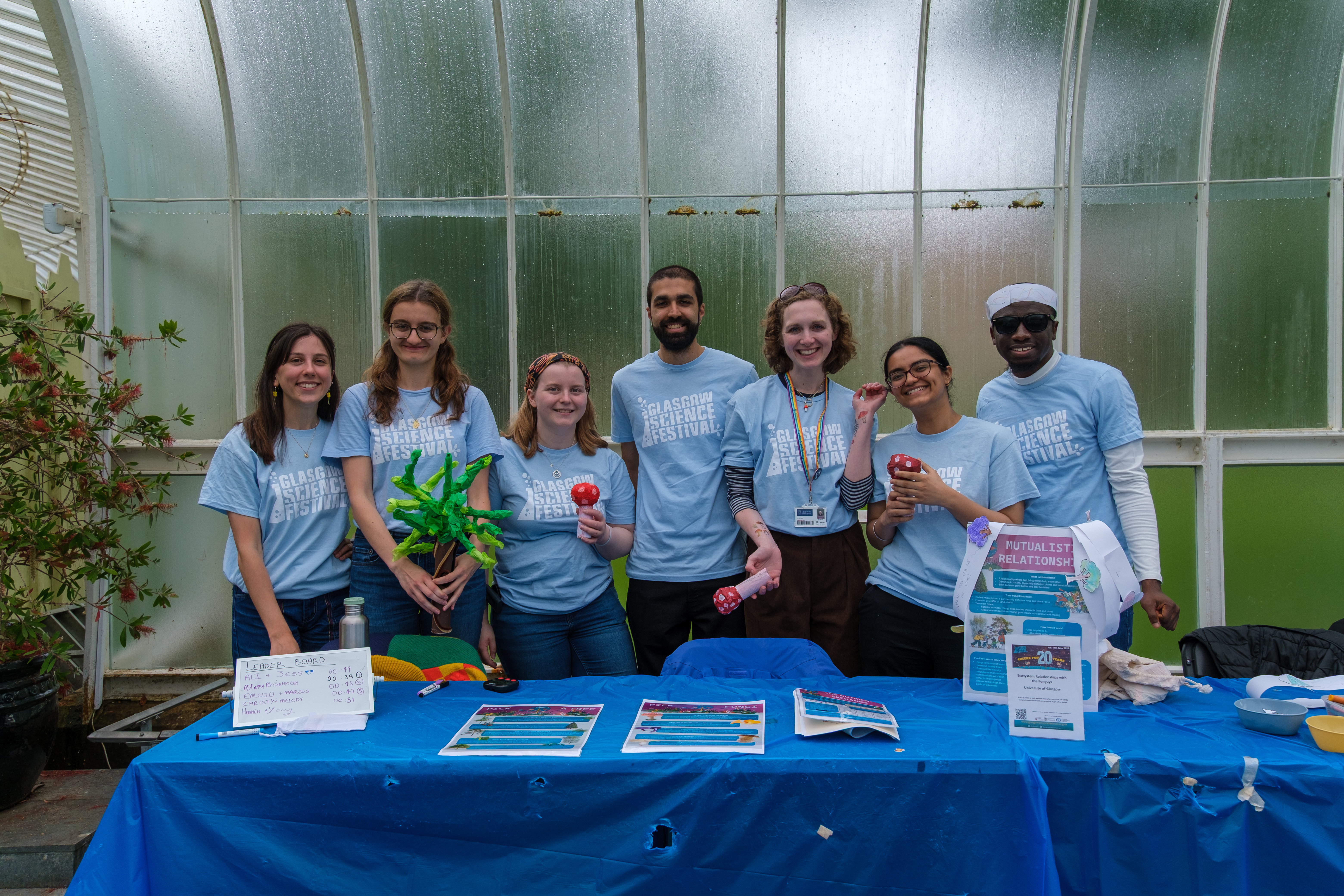 7 students in Glasgow Science Festival t-shirts standing at a table delivering an activity.