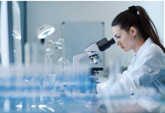 Female scientist wearing a lab coat looking down a microscope on a lab bench