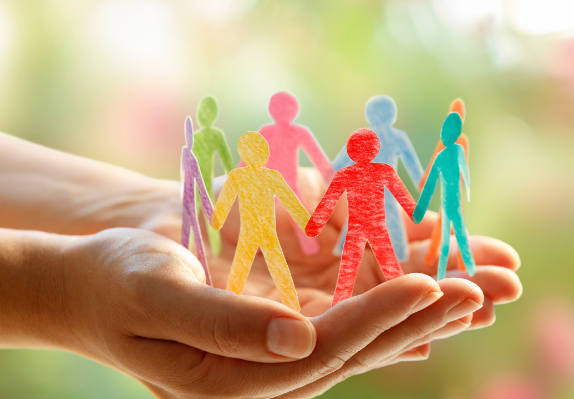A pair of hands holding multicouloured paper cut outs of people holding hands