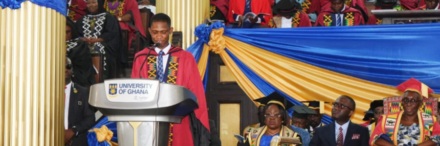 Worlanyo Tashie, wearing red and black academic robes, delivers the valedictory address from a University of Ghana lectern, surrounded by seated university officials and fellow graduates in the decorated Great Hall.