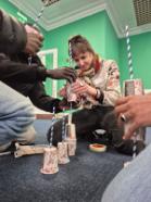 A group of people collaboratively building a tower from paper cups and straws during a workshop.