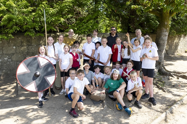 A class of children with their teacher stand in a playground part of an archaeology pilot