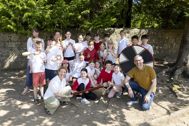 A group of children with their teacher stand in a playground as part of an archaeology pilot project