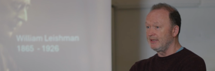 Professor Mike Barrett speaking beside a presentation slide showing Sir William Leishman and the dates 1865–1926.