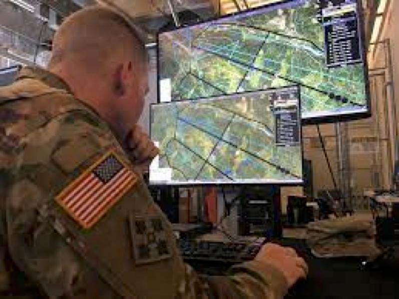 A view from behind of a US soldier studying detailed maps on computer screens