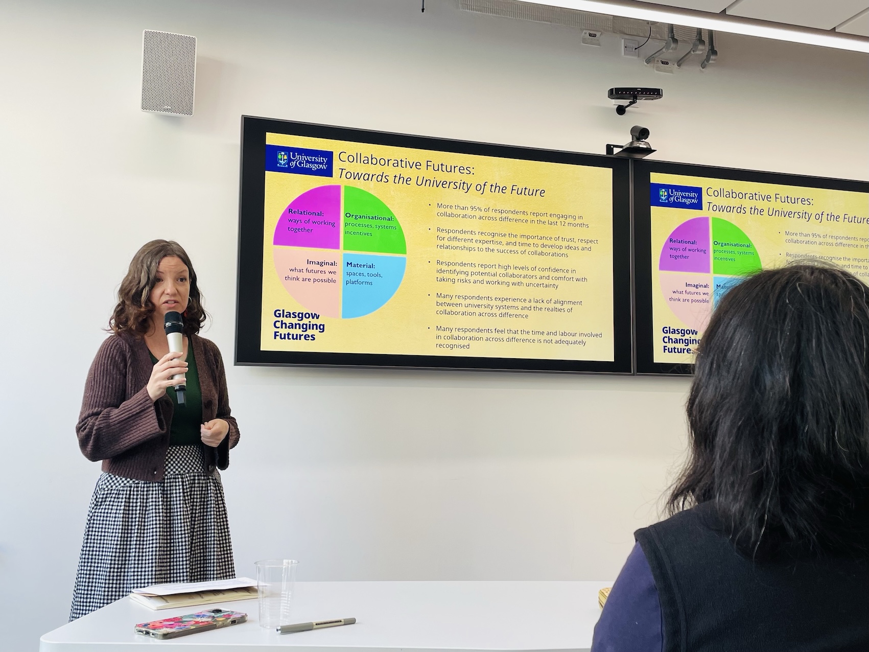Woman delivering a lecture; a screen behind her displays text and images