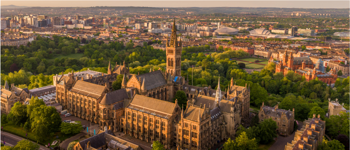 A drone shot of the gilbert scott tower at sunset with Kelvingrove Park in the background