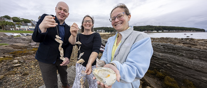 From left to right, Gillebrìde MacMillan, Dr Claire Ramjan and Dr Anna McGregor celebrate Project Eisirean in Millport where the new mobile oyster hatchery is based.