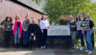 A group of School of Infection & Immunity colleagues stands outside the University of Glasgow’s Scottish Centre for Ecology and the Natural Environment. Director of Education Professor Nicola Veitch stands at the centre in white t-shirt and her hand on the sign